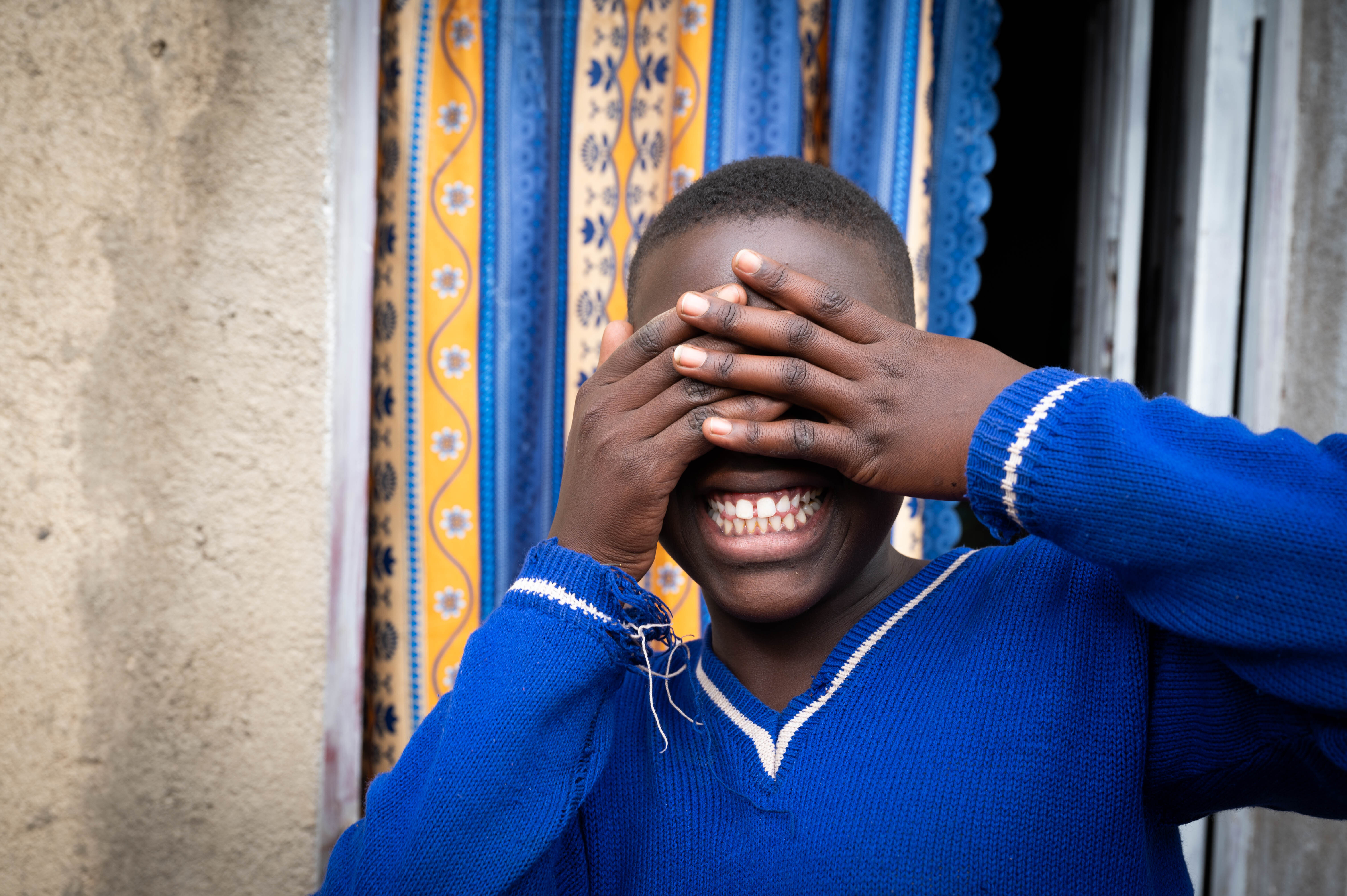 Nadine fra Rwanda holder hendene foran øynene og smiler